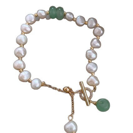 Gold-tone bracelet with white faux pearls and green beads lying on a satin surface
