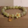 Green jade bead bracelet with gold-tone flower and square Fu charm on a beige box
