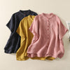 Three women's cotton linen short sleeve shirts in pink, yellow, and navy blue laid flat.