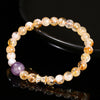 Close up view of a beaded bracelet made of golden rutilated quartz and a purple amethyst stone