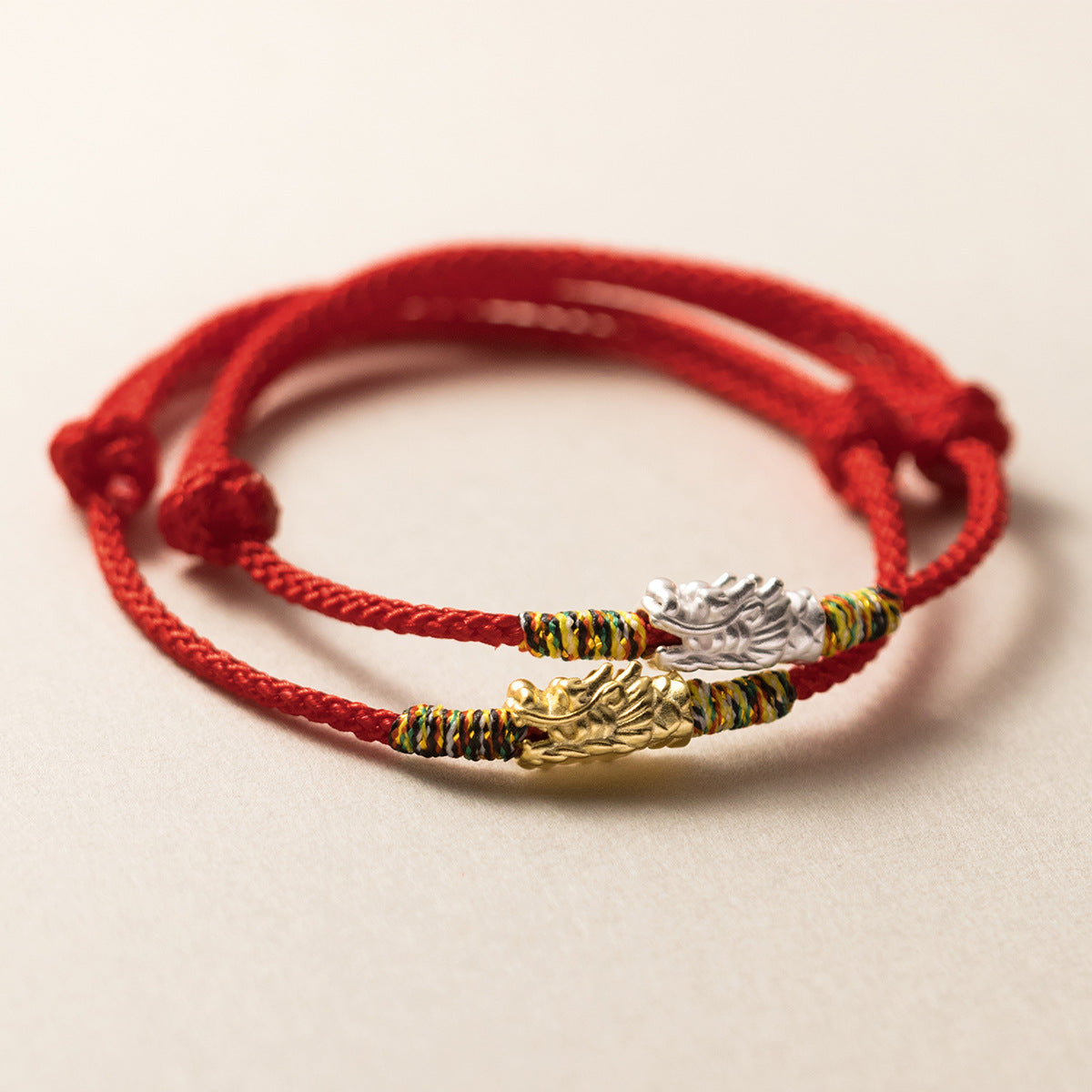 Close-up of a red woven bracelet with a silver dragon charm and colorful thread accents