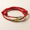 Close-up of a red woven bracelet with a silver dragon charm and colorful thread accents