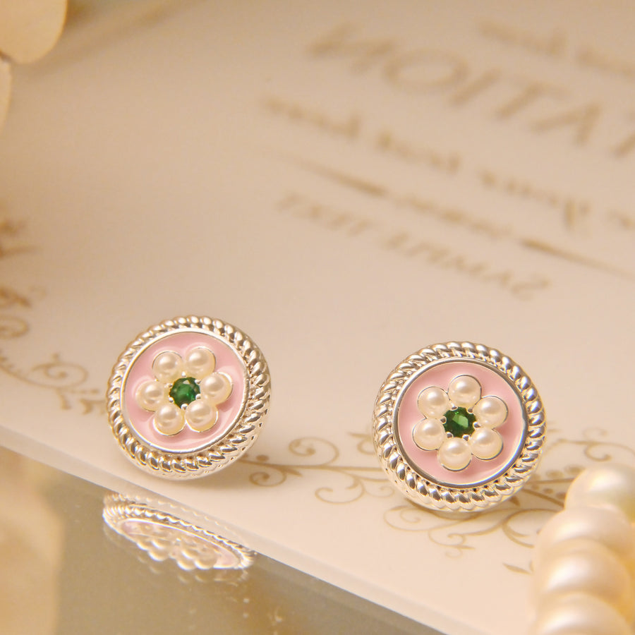 Close up of round copper stud earrings with pink enamel and a flower design