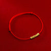 Close up of a red string bracelet with small textured gold beads on a red background