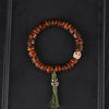 Close up of a brown bone bead bracelet with a white skull bead and green tassel on a black background
