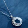 Close up of a silver koi fish pendant on a white stone circle against a blue background