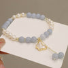 Close-up of an aquamarine and pearl beaded bracelet with a butterfly charm on a wrist.