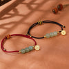 Close up of a braided bracelet with three pale green jade beads and a gold charm on a warm background