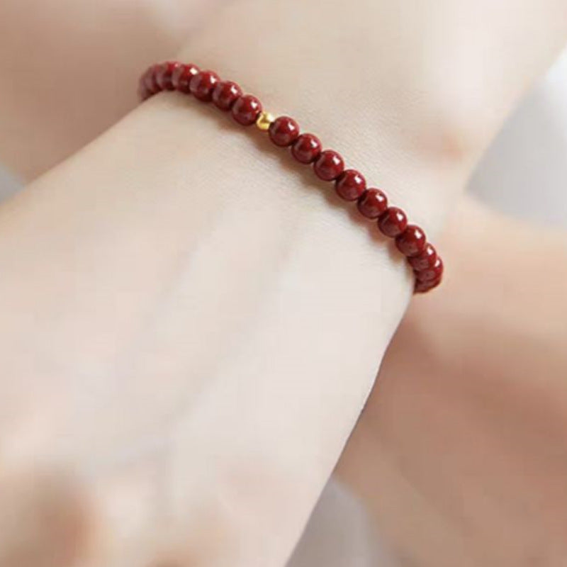 A woman's wrist wearing a thin red cinnabar bead bracelet with one small gold bead.