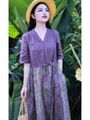 Woman wearing a purple cotton linen midi dress with a floral skirt in a garden setting