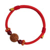 Close up of a red braided bracelet with a round wooden bead carved with a horse face