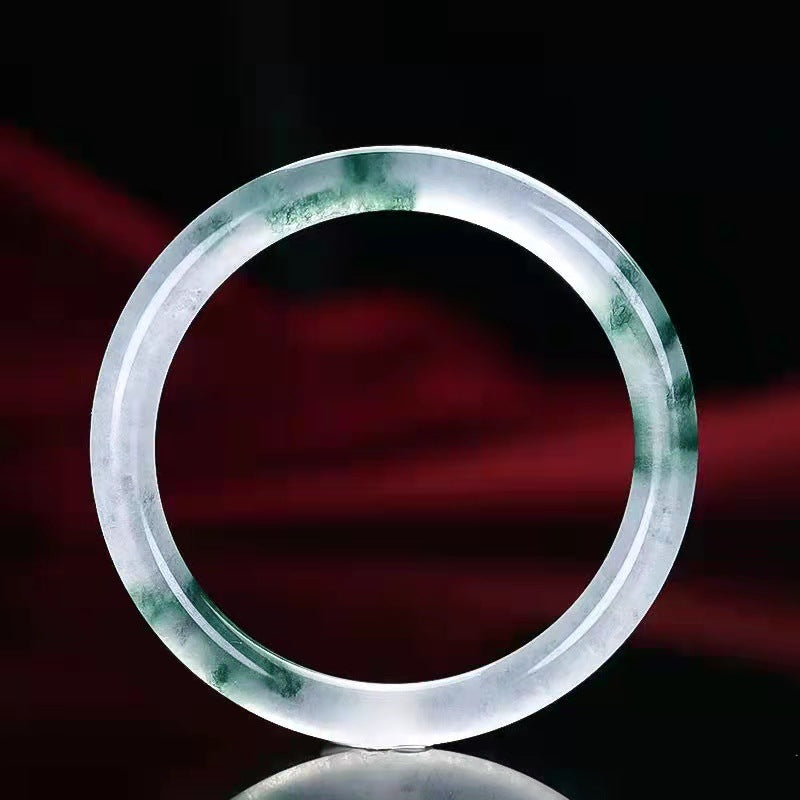 Close up of a translucent white jade bangle with green floating flower patterns