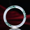 Close up of a translucent white jade bangle with green floating flower patterns