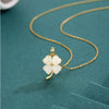 Gold tone sterling silver necklace with a white four leaf clover jade pendant on a teal background