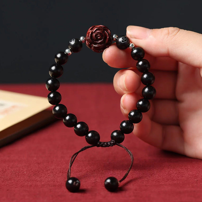 Close-up of a dark ebony wood beaded bracelet with a carved rose charm held in hand
