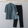 A teal green traditional Chinese style half sleeve top and black pants hanging on a wooden rack