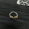 Close up of an open ring with a textured silver band and two gold-tone skulls facing each other