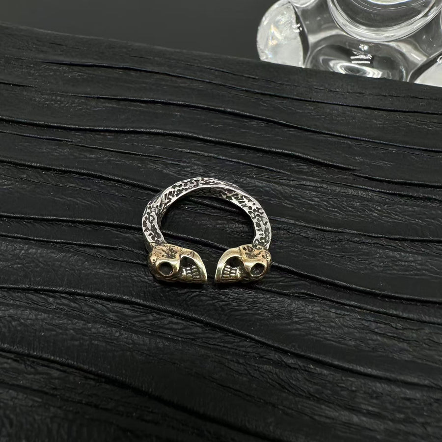 Close up of an open ring with a textured silver band and two gold-tone skulls facing each other