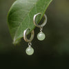 Silver-tone copper hoop earrings with a single round green simulated jade bead hanging below