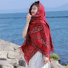 Woman wearing a red Tibetan style paisley shawl with tassels by the ocean