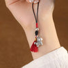 Hand holding a copper horse phone charm with a red tassel and black cord