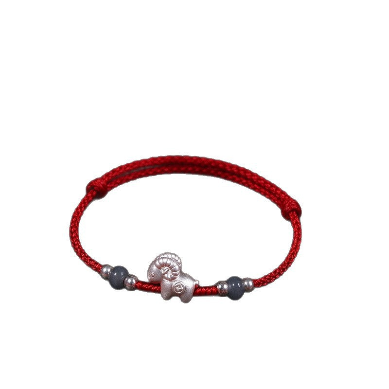 A red woven cord bracelet with a central silver goat charm and two dark beads