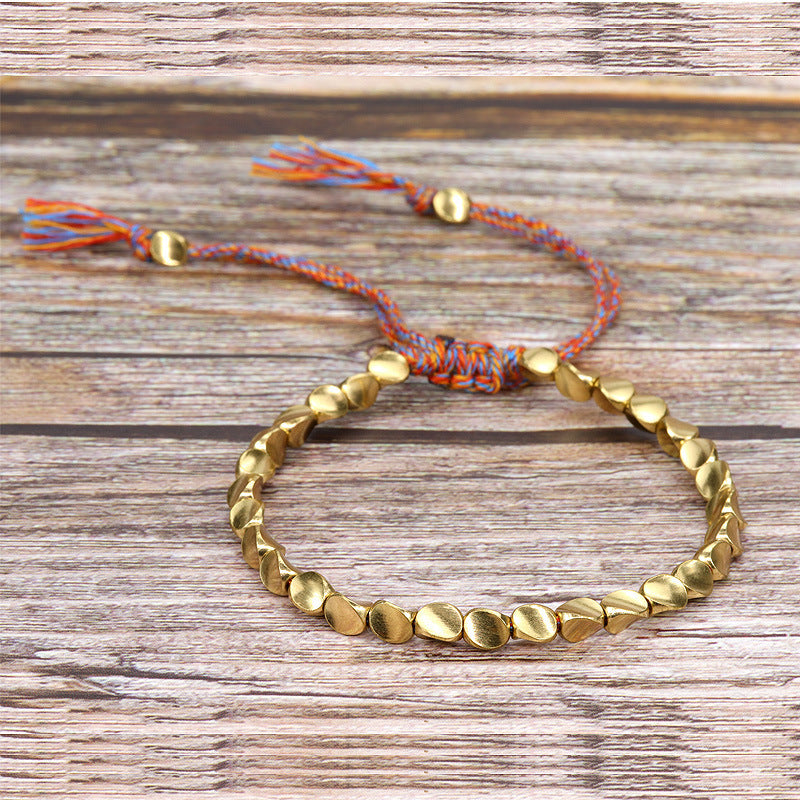 Gold-tone copper bead bracelet with multicolor woven cord on wood background