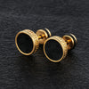Close-up of two round stud earrings with a black center and gold-tone rim on a dark textured surface
