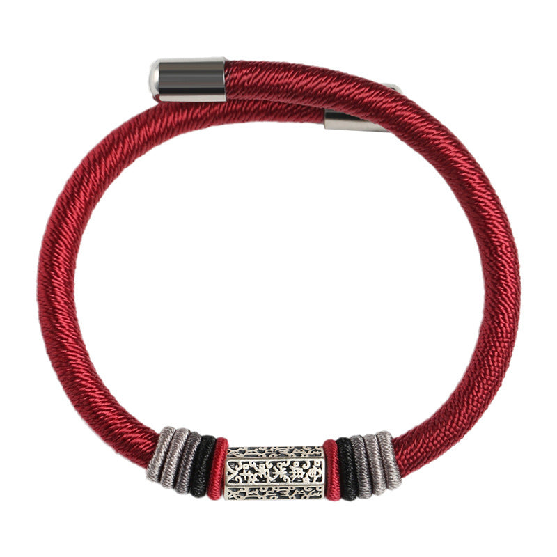 Close up of a wrist wearing a red woven bracelet with a silver mantra tube