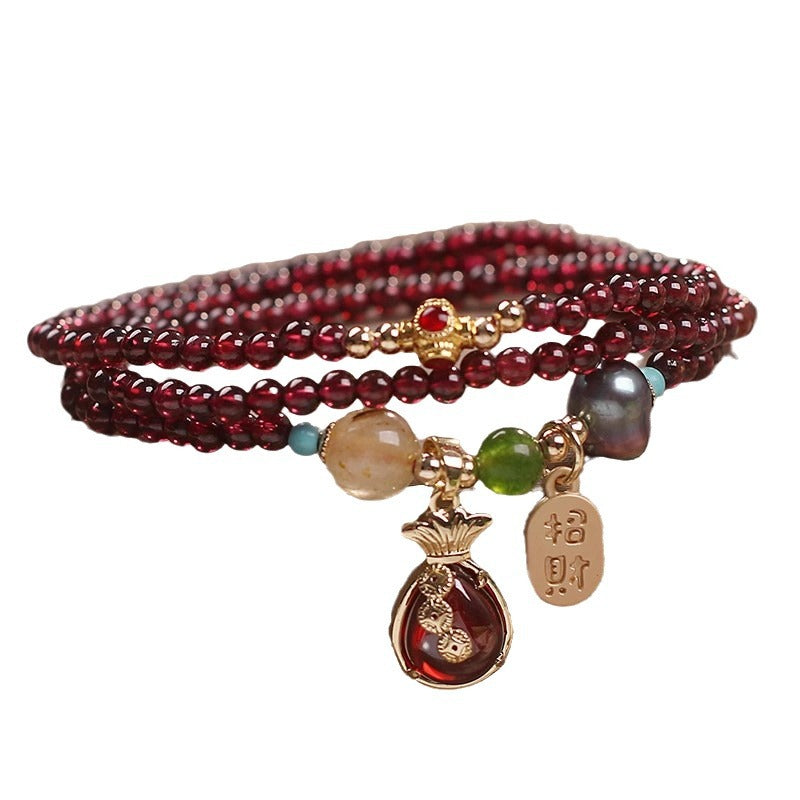 Close up of a multi layered wine red garnet bracelet with gold money bag charm