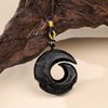 Close up of a black obsidian swirl pendant hanging from a dark cord against wood