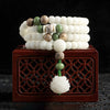 White bodhi seed mala with green accents and a carved lotus pendant resting on a wooden box
