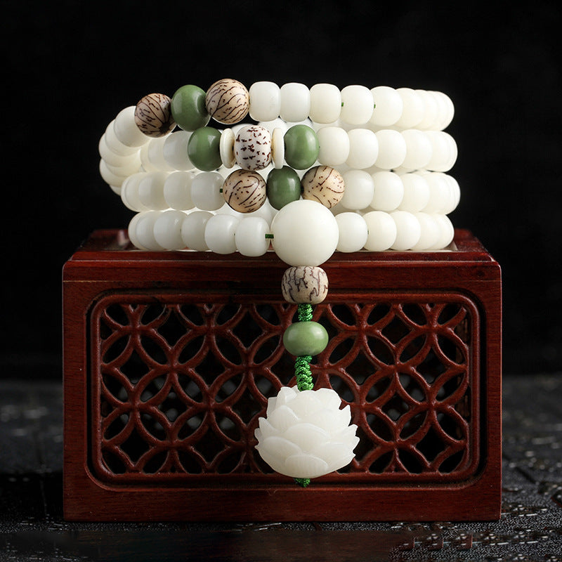 White bodhi seed mala with green accents and a carved lotus pendant resting on a wooden box