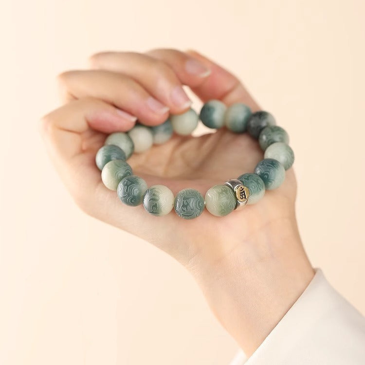 Hand holding a green gradient bodhi seed bracelet with engraved beads and a gold charm