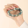Hand holding a green gradient bodhi seed bracelet with engraved beads and a gold charm