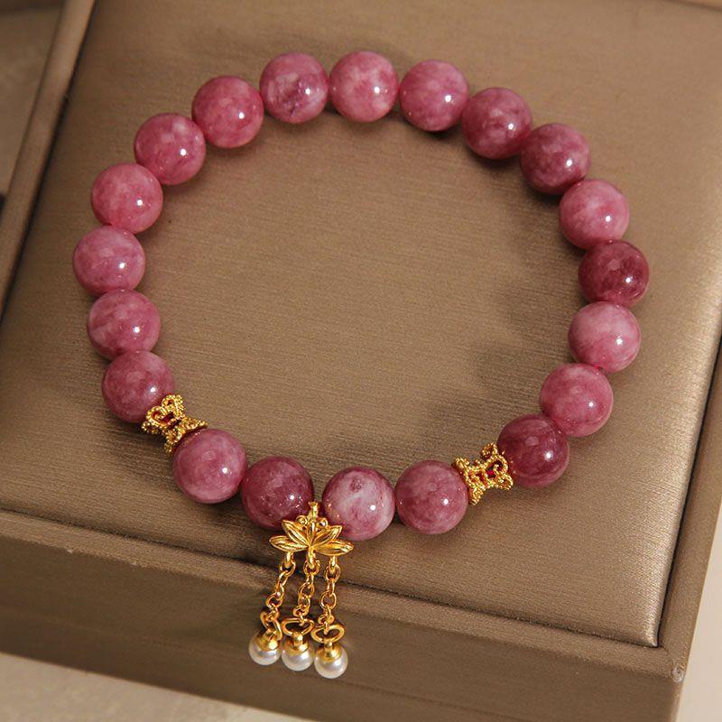 Pink tourmaline beaded bracelet with gold lotus charm and pearl tassel on a box