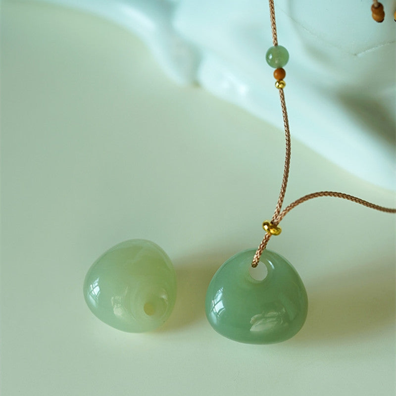 Green jade lock pendant hanging on a thin brown cord with small accent beads