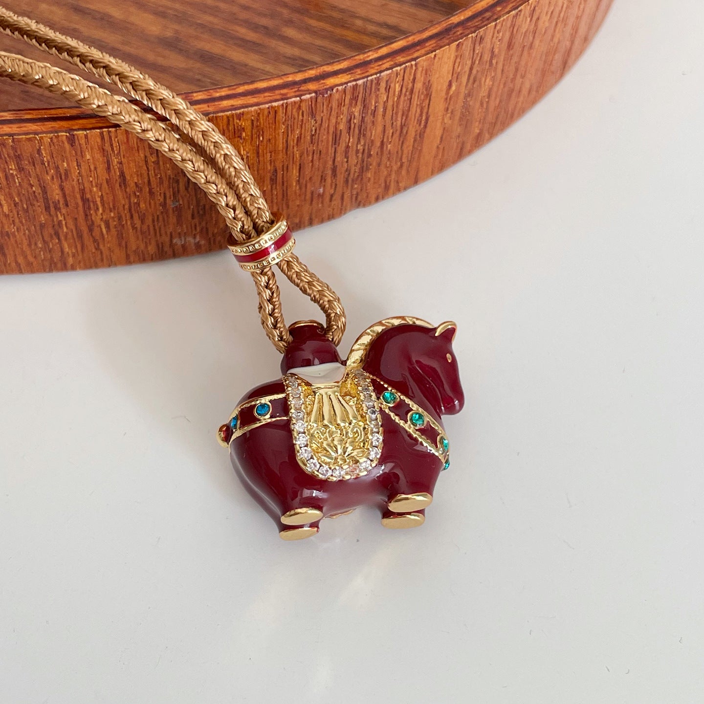 Close up of red enamel horse pendant on gold tone braided chain