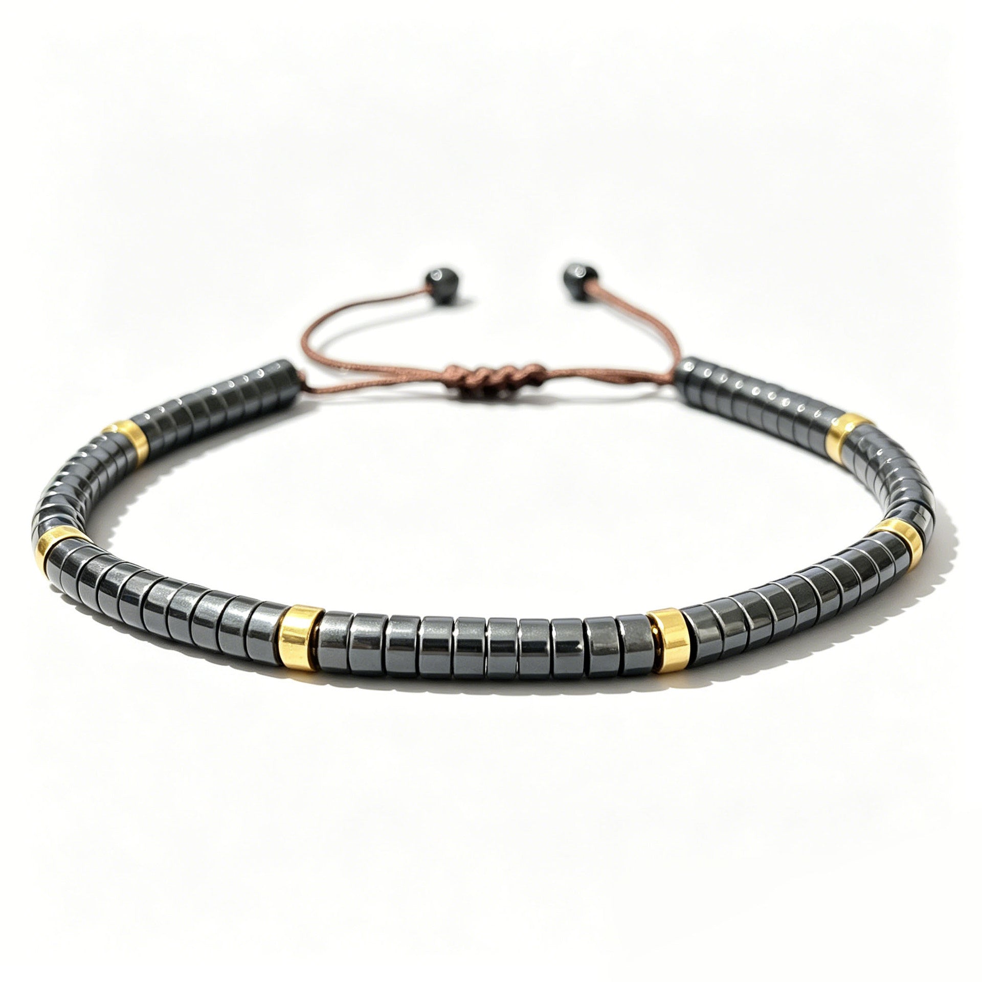 Close up of a dark grey natural stone bracelet with gold tone spacers and brown cord