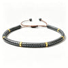Close up of a dark grey natural stone bracelet with gold tone spacers and brown cord