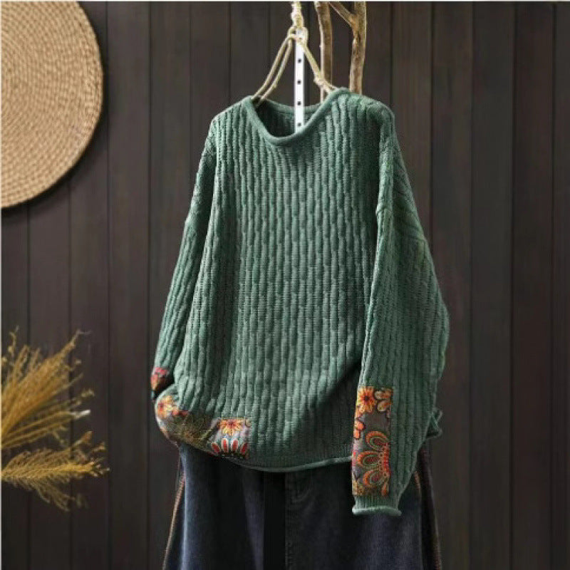 Green long sleeve crew neck women's sweater with floral patchwork details hanging on a wooden hanger