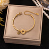 Gold-tone titanium steel bracelet with heart and coin charms in a beige box