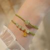 Green woven bracelet with light green beads and a gold-tone bell charm worn on a wrist