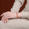 Close up of a wrist wearing a red string bracelet with a small green jade bead and gold charm