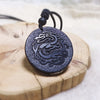 Round black shungite stone pendant with a carved dragon design on a wooden surface