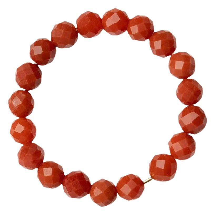 Close up of a faceted red orange stone ring on white background