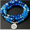 Close-up of a blue agate mala bracelet wrapped around a wrist with a silver lotus pendant