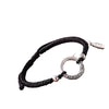Close up of a black cord bracelet with a silver ring and charm on a wrist