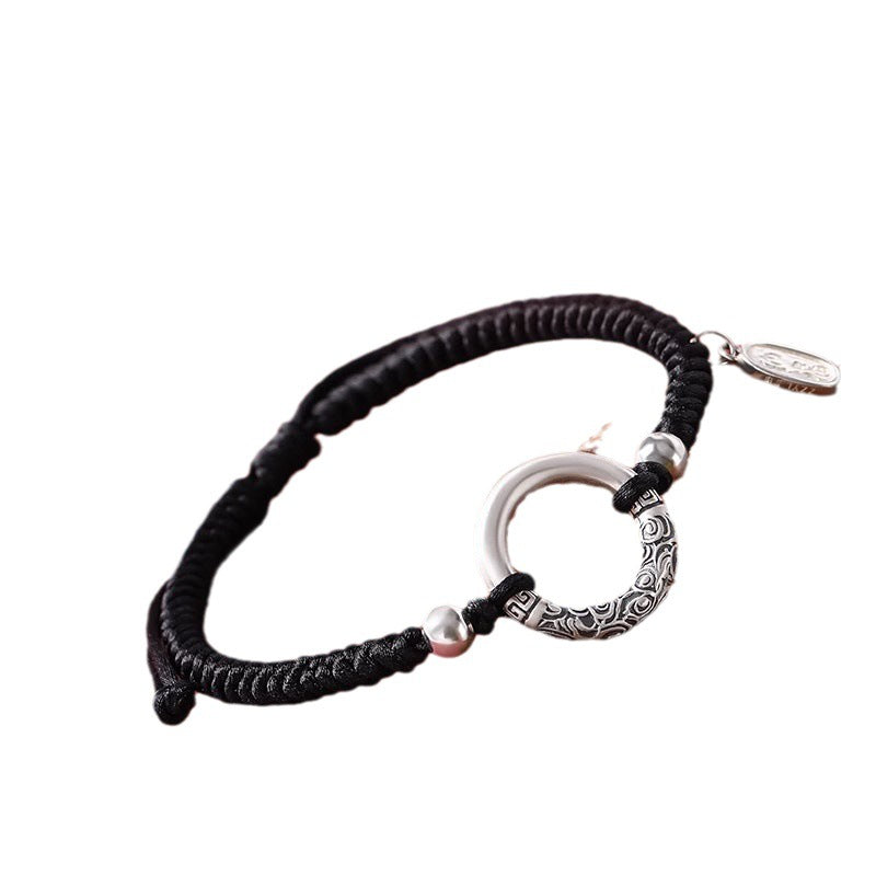 Close up of a black cord bracelet with a silver ring and charm on a wrist