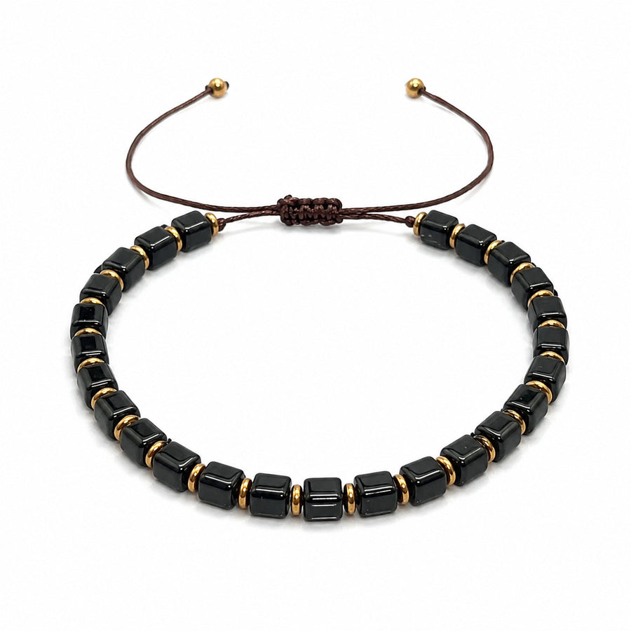 Black obsidian square bead bracelet with gold tone spacers on a dark background